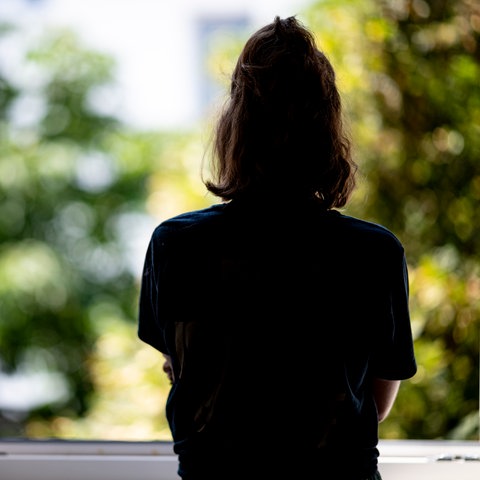 Frau steht am offenen Fenster und schaut raus. Wie sehen sie von hinten.