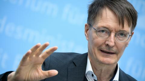 Ein Mann im Anzug und mit Brille steht bei einer Pressekonferenz vor einer blauen Wand.