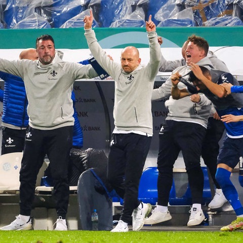 Jubelnden Fußballspieler und -trainer am Spielfeldrand.