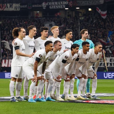 Eine Fußballmannschaft in weißen Trikots hat sich für ein Foto auf dem Fußballfeld gruppiert und alle posieren für die Kamera.