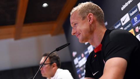 Sebastian Rode sitzt bei einer PK im Trainingslager vor einem Mikrofon und lächelt.