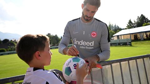 Kevin Trapp unterschreibt auf einem Ball, den ihm ein kleiner Junge hinhält