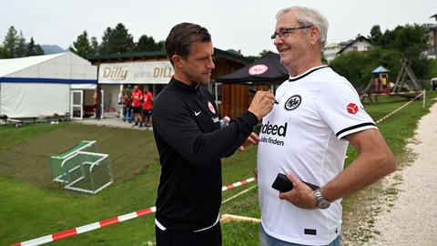 Markus Krösche unterschreibt auf dem Triko eines weißhaarigen Mannes mit Brille