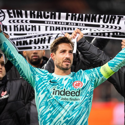 Kevin Trapp hält einen Schal der Eintracht in die Höhe.